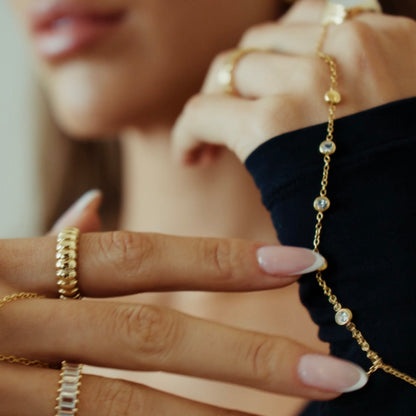 A close-up lifestyle shot of a woman wearing delicate gold jewelry, including a gold hand chain bracelet with 5 clear cz crystal beads on her wrist and matching gold rings on her fingers.