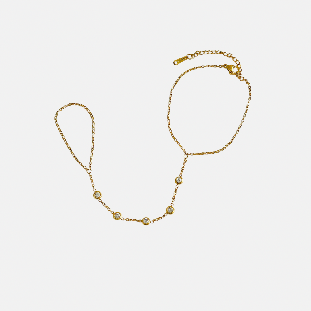 A delicate gold handchain featuring five small, bezel-set round clear cz stones spaced evenly along the chain, displayed on a light gray background.